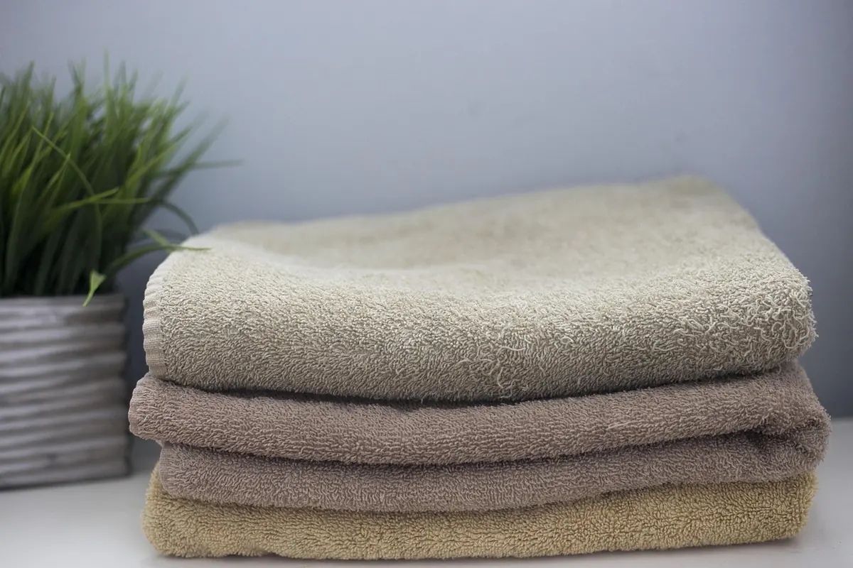 Stack of folded beige towels beside a potted plant